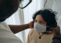 Crop man putting medical mask on face of ethnic child Free Stock Photo