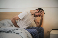 man getting up from bed holding his head.
