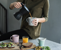 Woman in Green Top Pouring Coffee in a White Mug Free Stock Photo